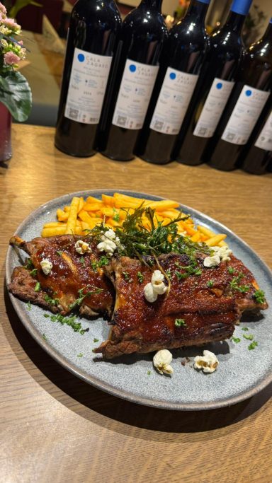 Gegrilltes Fleisch mit Beilagen, garniert mit Kräutern und Popcorn, umgeben von Weinflaschen.