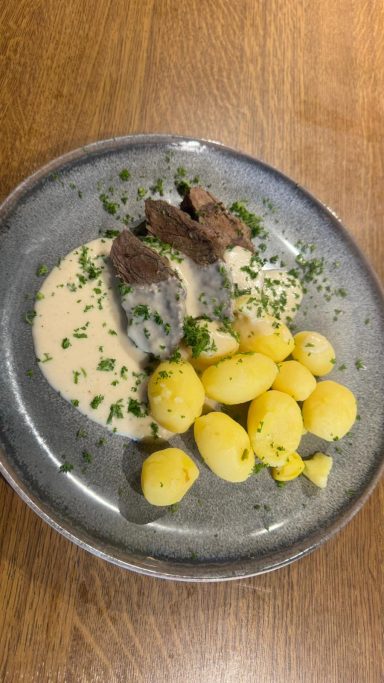 Teller mit Tafelspitz, Sauce und Kartoffeln, garniert mit frischen Kräutern.