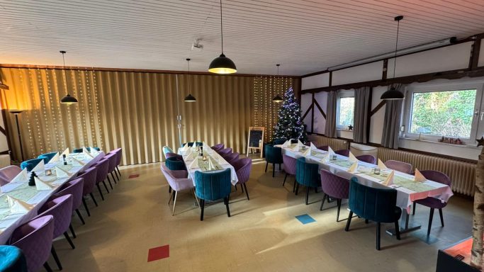 Gemütlicher Speiseraum mit gedeckten Tischen in lila und blauen Stühlen.